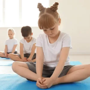 Kinder sitzen im Schneidersitz auf Matten im Bewegungskurs