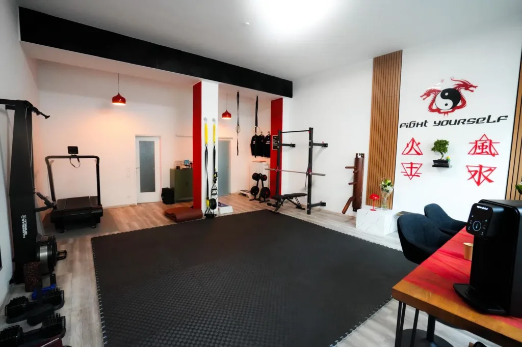 Trainingsflaeche im Studio Lehel mit Matte, Kraftgeraeten und dem Fight Yourself Logo an der Wand